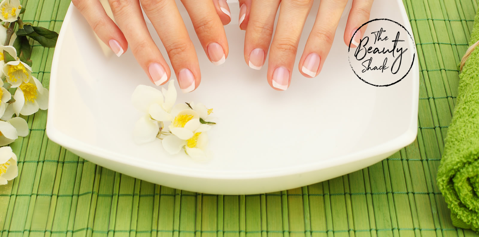 Hands and a bowl of liquid for soaking nails during manicure - The Beauty Shack Salon Logo